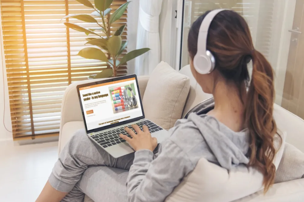 A language learner wearing headphones speaks along to a video on their laptop, practising pronunciation through the shadowing technique